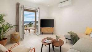 Een moderne woonkamer met een grote televisie, een bank, een salontafel en een balkon met uitzicht.