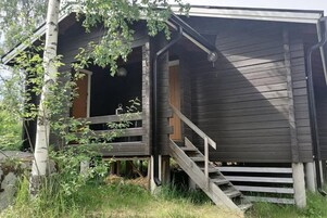 Una cabaña rústica con una escalera de madera que conduce a una puerta, rodeada de árboles y césped.
