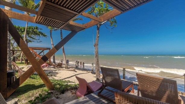 Een uitzicht op het strand met houten ligstoelen, een beschaduwd gedeelte en palmbomen.