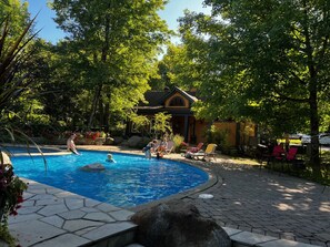 A swimming pool surrounded by trees and a building with a sloped roof. - Le Cerf Blanc 3BDR Manoirs-Tremblant (Mont-Tremblant)