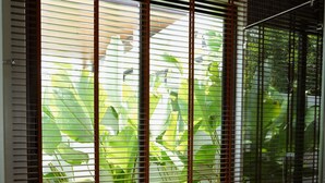Un baño moderno con una bañera independiente, persianas de madera y vistas a exuberante vegetación.