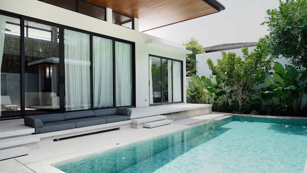Una casa moderna con piscina, amplios ventanales de vidrio y techo de madera.