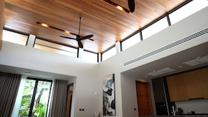 Un interior moderno con techos altos, vigas de madera, ventiladores de techo, ventanas grandes y una zona de cocina.