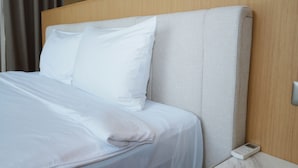 Una cama bien hecha con sábanas y almohadas blancas, un cabecero de madera y un panel de control junto a la cama.