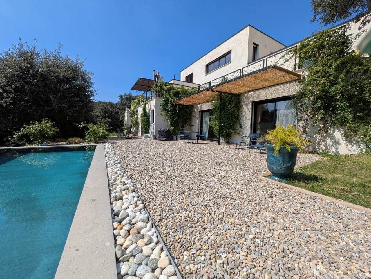 Una casa moderna con piscina, un patio con mobiliario exterior y un jardín.