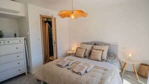 Une chambre à coucher comprenant un lit, des tables de chevet, une commode et un luminaire suspendu.