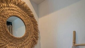Une salle de bain avec un meuble-lavabo en bois, un vasque en pierre, un miroir tressé et un porte-serviettes.