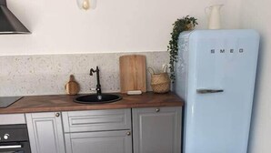 Une cuisine avec une table en bois, un panier de produits frais, un réfrigérateur de style rétro et un luminaire suspendu.