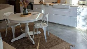 Une cuisine moderne avec des meubles blancs, une table de salle à manger ronde et deux suspensions.