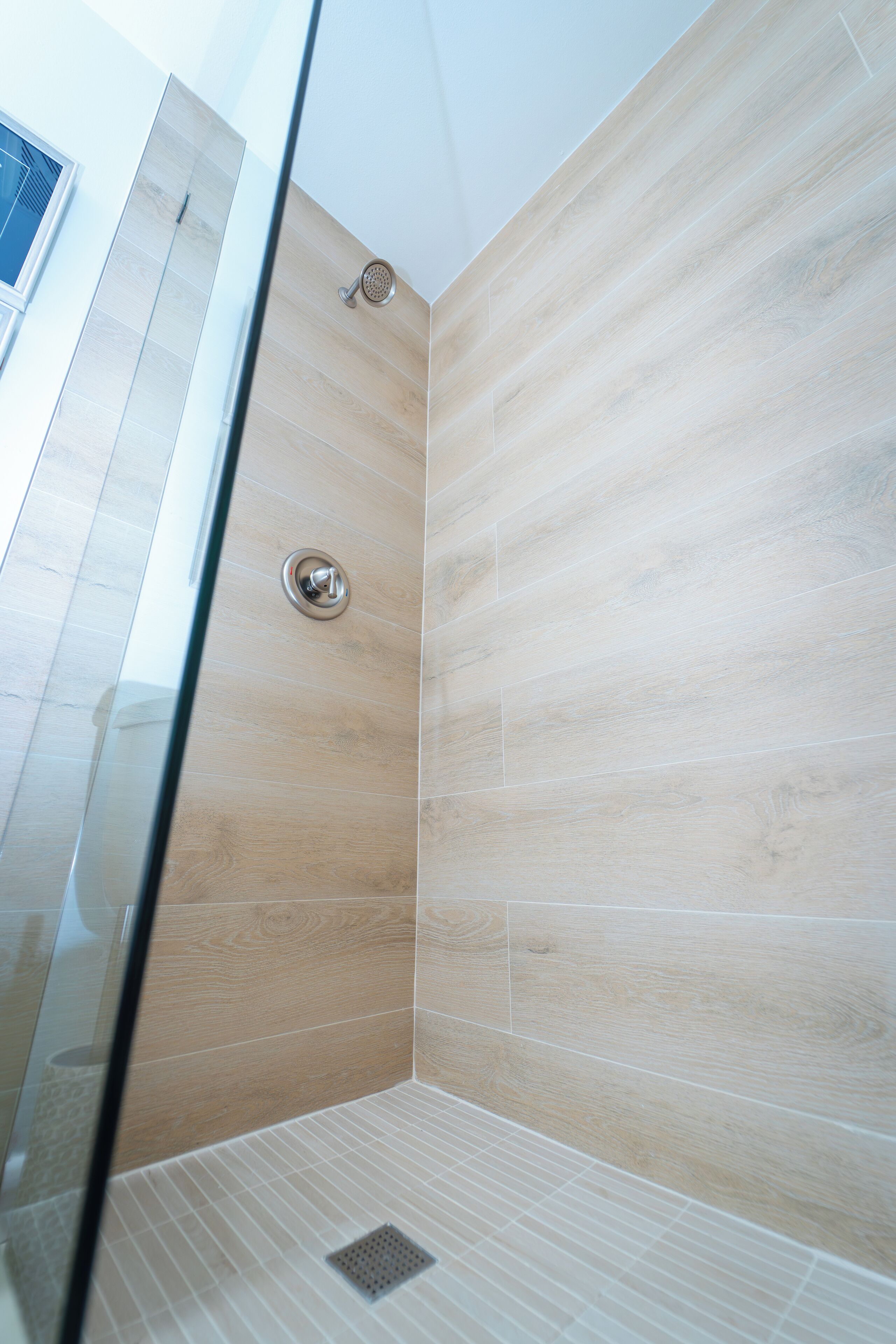 A modern shower with light wood paneling and a glass door.