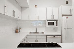 Una cocina moderna con armarios blancos, un lavamanos de acero inoxidable, un microondas y un lavavajillas integrado.