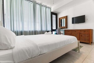 Habitación de hotel con una cama grande, un aparador de madera, un televisor montado en la pared y una ventana con cortinas.