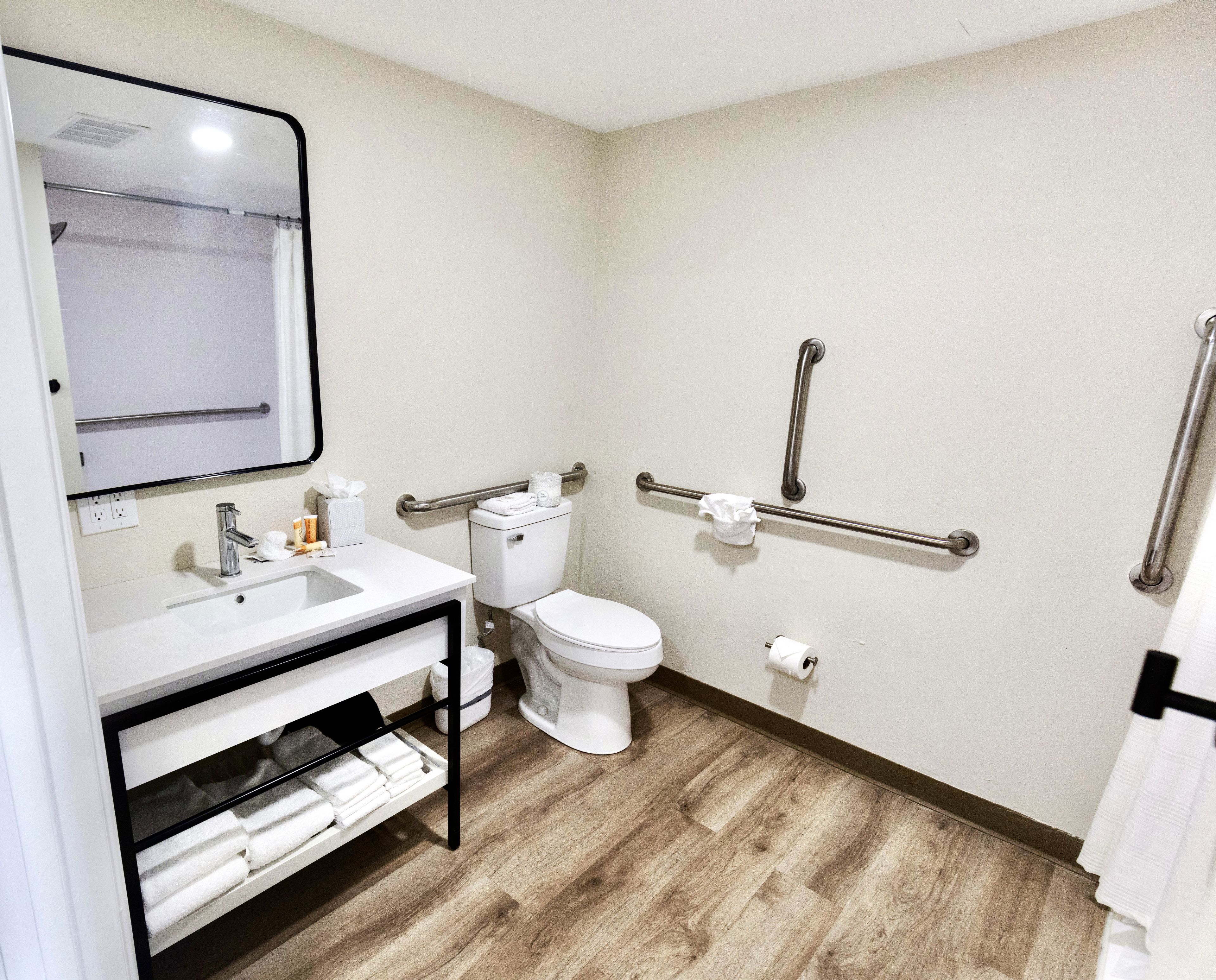 A small, clean bathroom with a white sink, toilet, and handrails for accessibility.