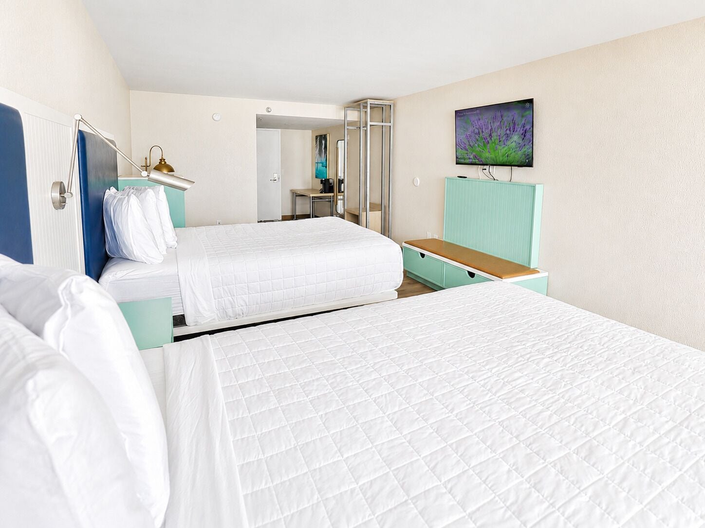 A hotel room with two beds, a television, a desk, and a bathroom visible through an open door.