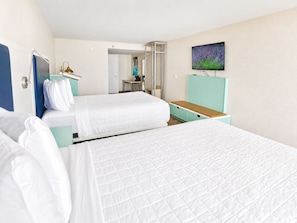 Ein Hotelzimmer mit zwei Betten, einem Fernseher, einem Schreibtisch und einem durch eine offene Tür einsehbaren Badezimmer.