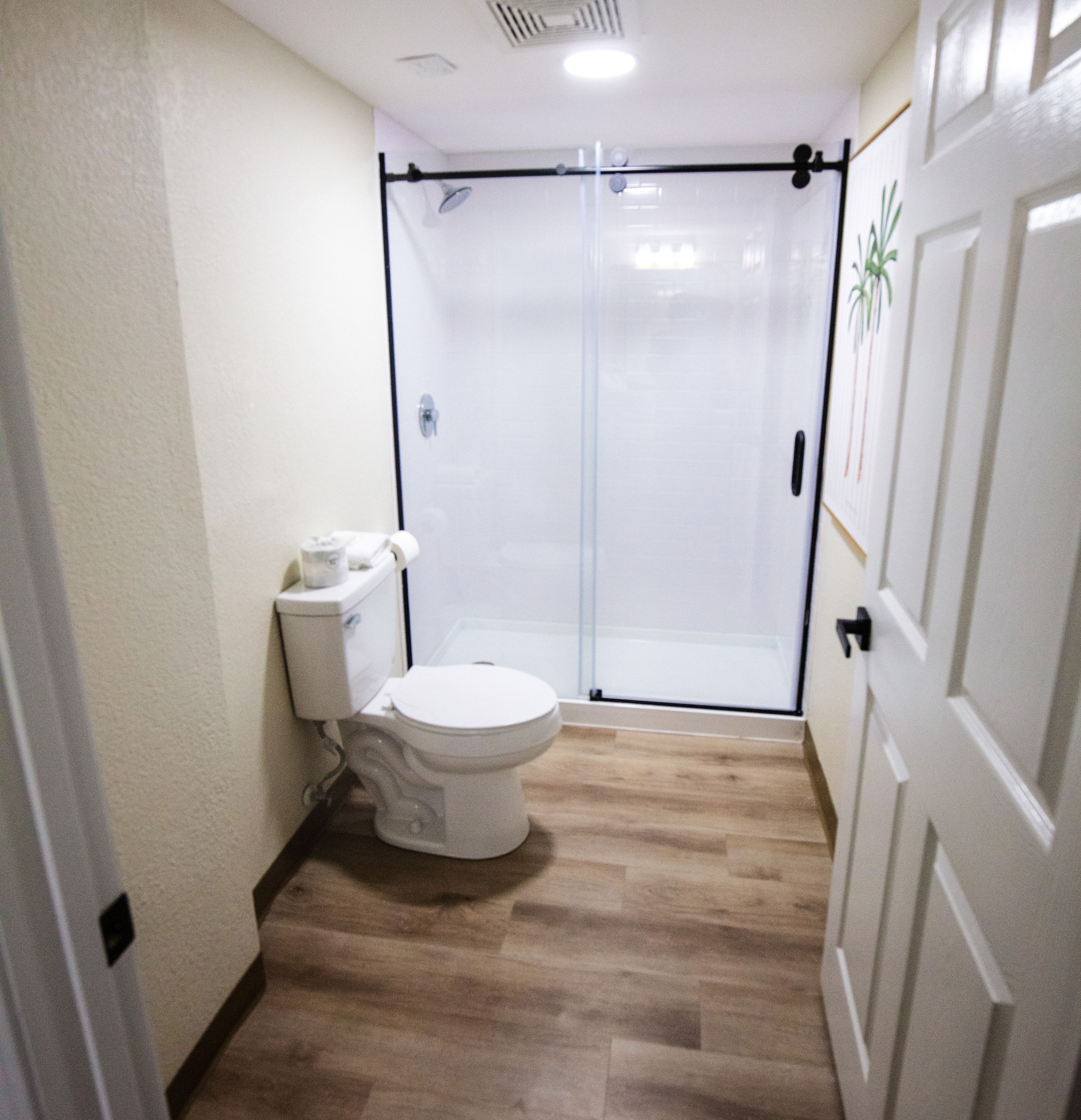 A bathroom with a toilet, a shower enclosure, and a wooden floor.