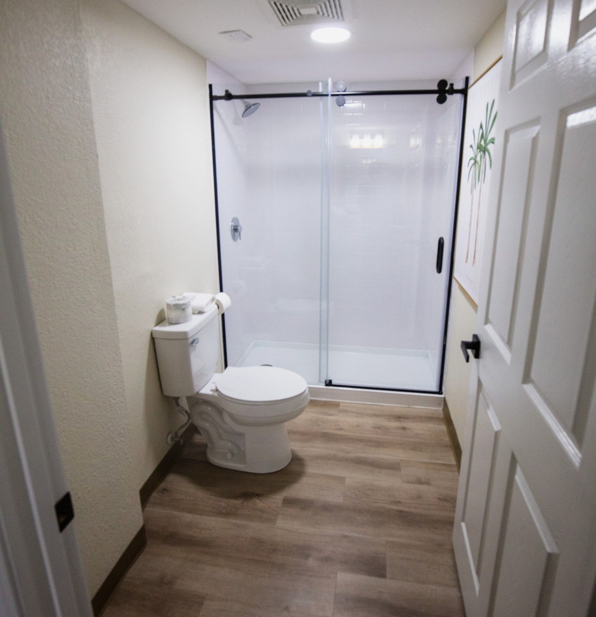 A bathroom with a toilet, a shower enclosure, and a wooden floor.