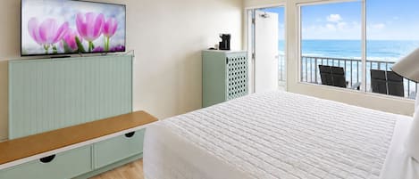A hotel room with a bed, a television on a stand, a view of the ocean through a balcony, and a wooden floor.