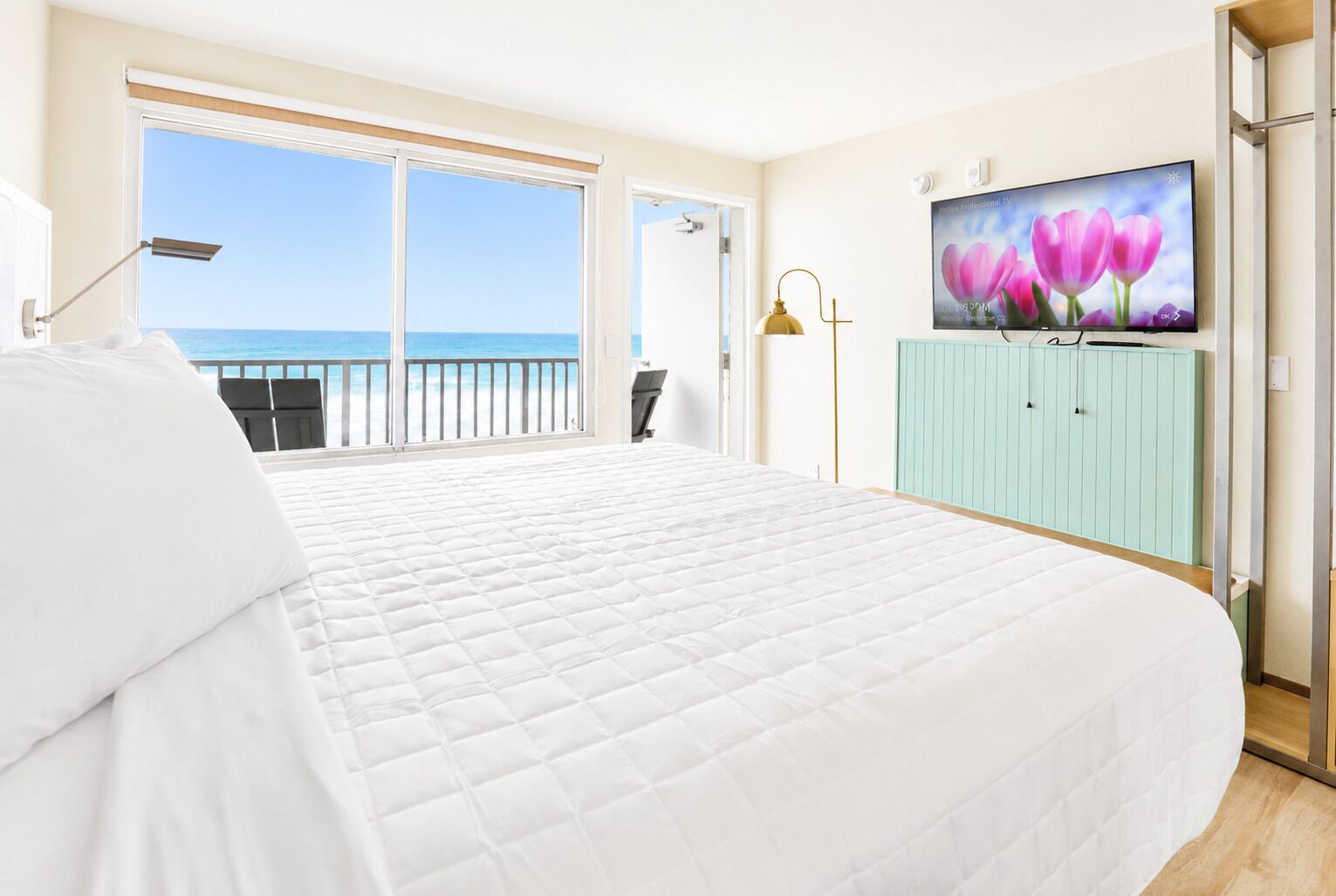 A hotel room with a large bed, a television, a view of the sea, and a balcony.