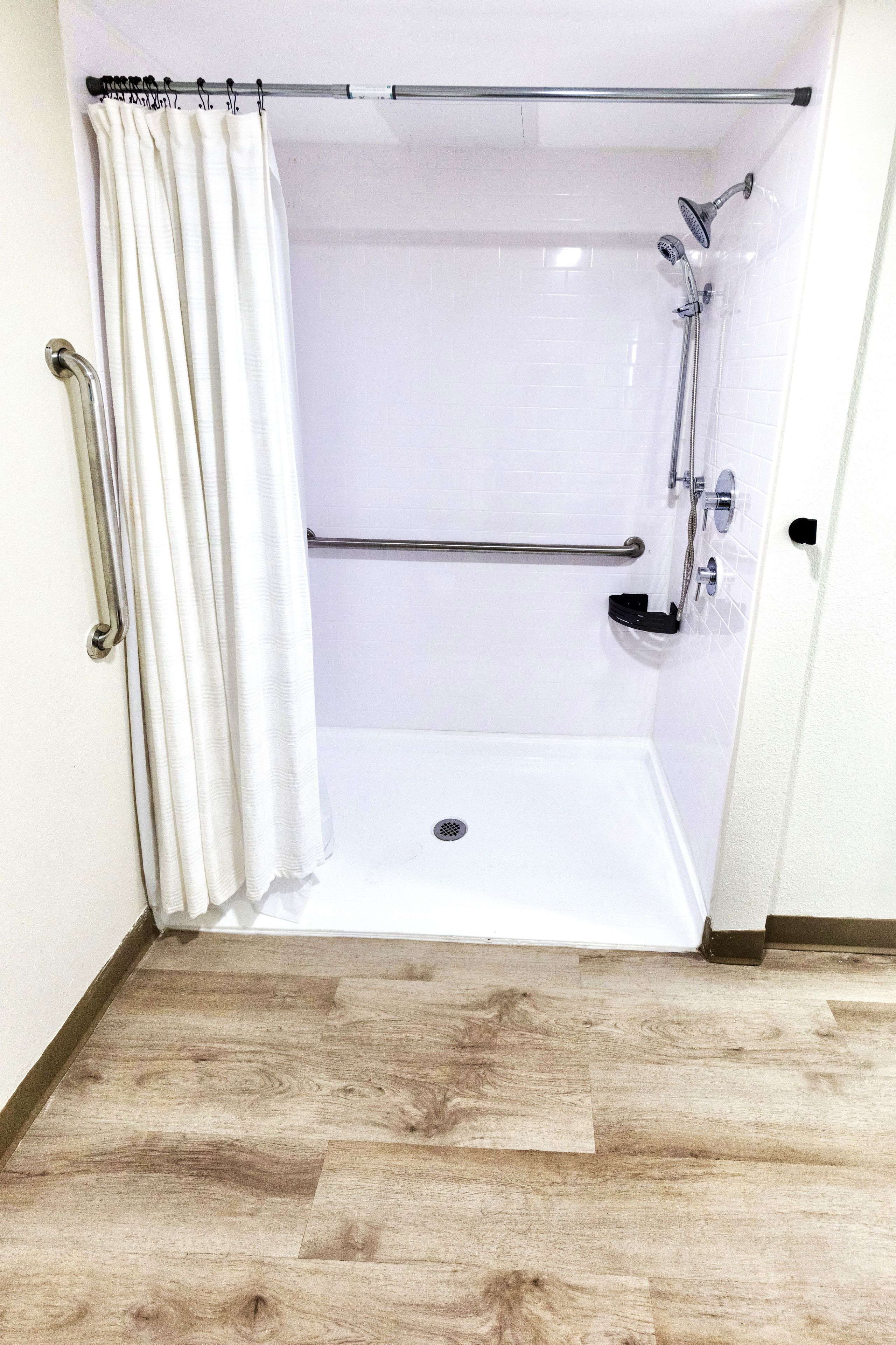 A modern bathroom with a shower, a handrail, and a tiled floor.
