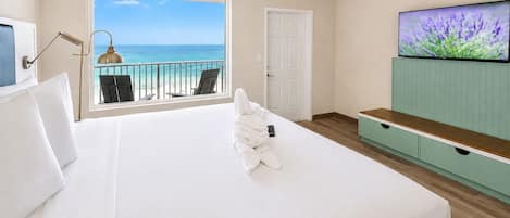 A hotel room with a bed, a TV, a balcony with chairs, and a view of the ocean.