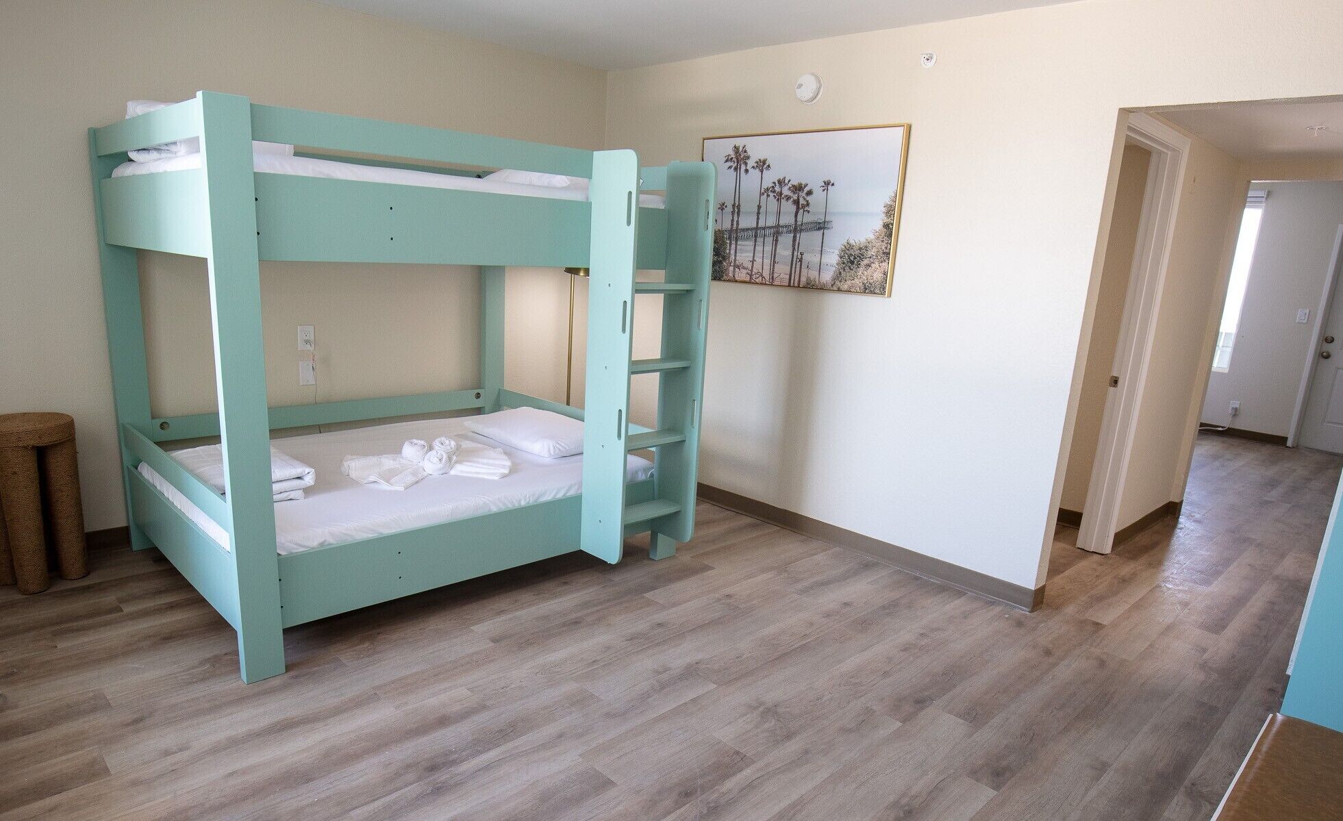 Uma cama beliche com roupa de cama branca, um quadro na parede e um chão de madeira.