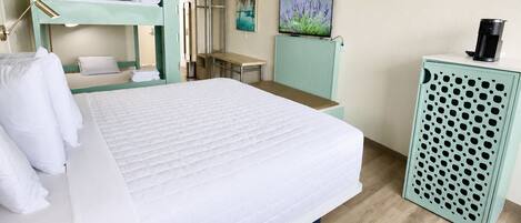 Een hotelkamer met een bed, bureau, spiegel, televisie en koffieapparaat.