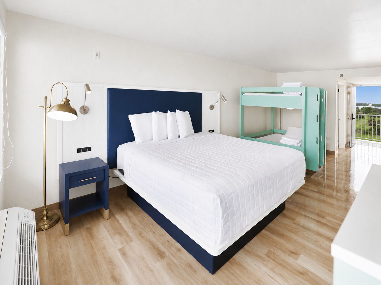 A hotel room with a large bed, a nightstand, a desk, a bunk bed, and a view of the outdoors.