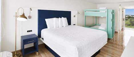 A hotel room with a large bed, a nightstand, a desk, a bunk bed, and a view of the outdoors.