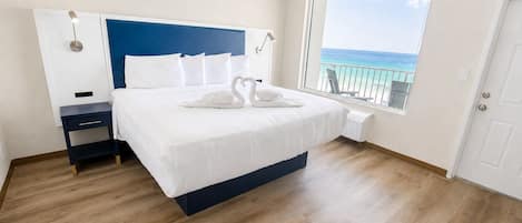 A bedroom with a bed, a nightstand, a window with a view of the ocean, and a door.