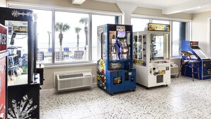 Una stanza con cabinati arcade, un'ampia finestra vista palme e un pavimento piastrellato.