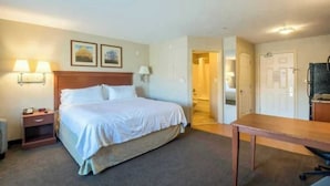 A hotel room with a bed, bedside tables, a desk, and a chair. There are two lamps on the wall, a door, and a window. - One Bedroom King suite ADA (Parachute)