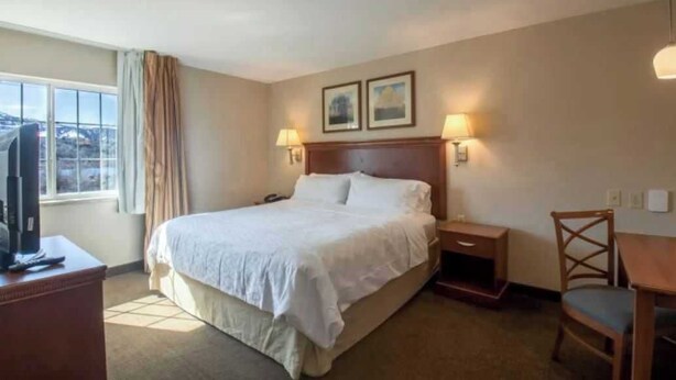 A hotel room with a large bed, a desk with a computer, a chair, and two bedside lamps. - One Bedroom King suite ADA (Parachute)