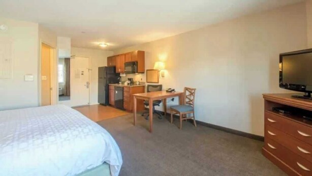 Een hotelkamer met een bed, een bureau, een stoel, een televisie en een kitchenette.