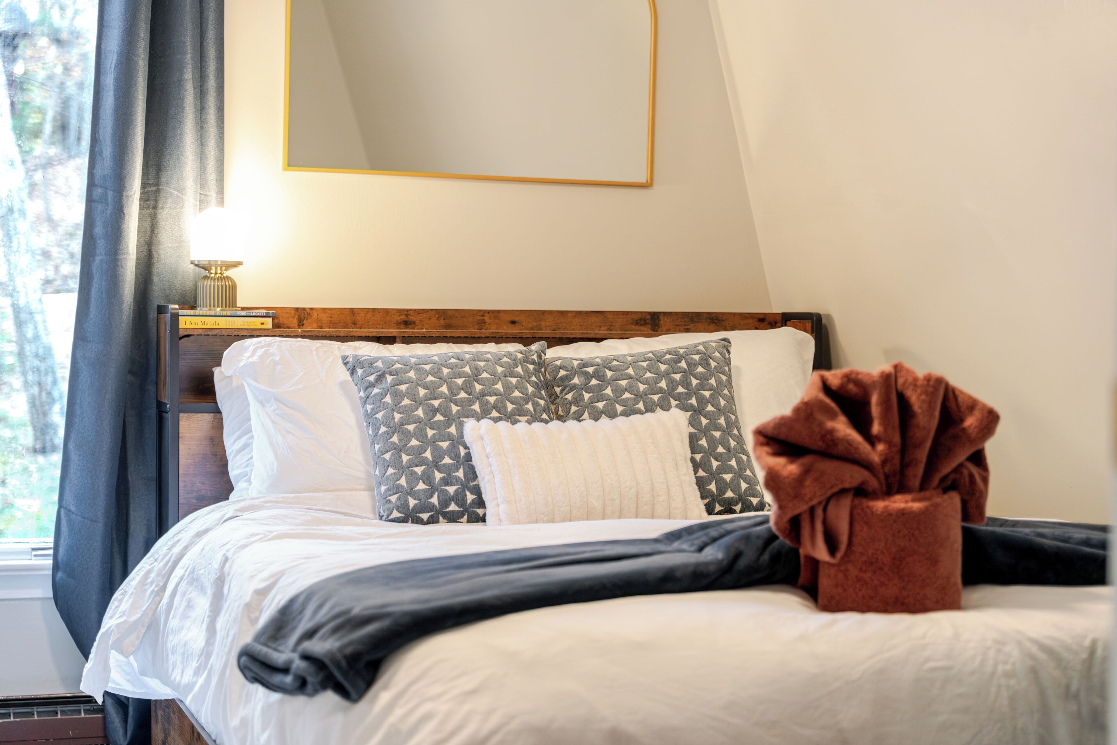 A neatly made bed with patterned pillows, a bedside lamp, and a brown towel on the bed.