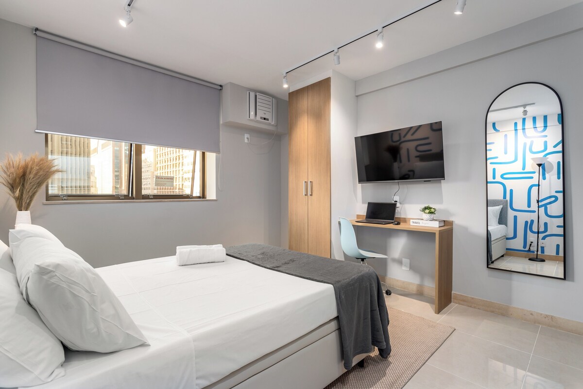 Une chambre moderne avec un lit, un bureau, une télévision et une grande fenêtre.