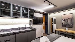 Une chambre d’hôtel moderne dotée d’un coin cuisine, d’un lit avec des serviettes, d’un bureau et d’une grande fenêtre.