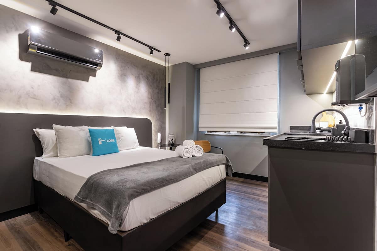 Quarto de hotel moderno com uma cama grande, escrivaninha embutida e janela com persianas.