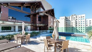 Un espace aménagé au bord de la piscine, avec des sièges extérieurs, et un bâtiment portant l’inscription « RELAXE & CONVIVIALITÉ ».