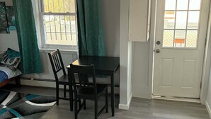 Una habitación con una mesa de comedor y sillas, una ventana con cortinas, una puerta y una cama con cabecera.