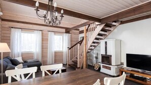 A cozy living room with a wooden staircase, a fireplace, a TV, and a dining area with a table and chairs. - Pyry Cottage (Muurame)