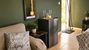 Una sala de estar con un sofá, una mesita con una planta, un refrigerador negro y un espejo montado en la pared.