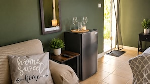 Een woonkamer met een bank, een klein tafeltje met een plant, een zwarte koelkast en een spiegel aan de muur.