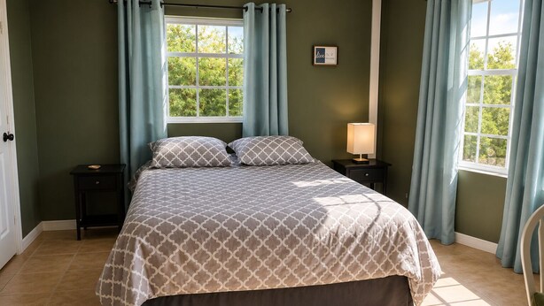 Un dormitorio con cama, mesitas de noche, ventana y cortinas.