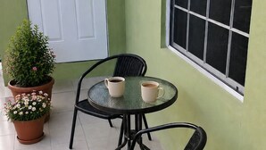 Un pequeño patio con una mesa redonda y dos sillas, una puerta blanca y una ventana con vistas.