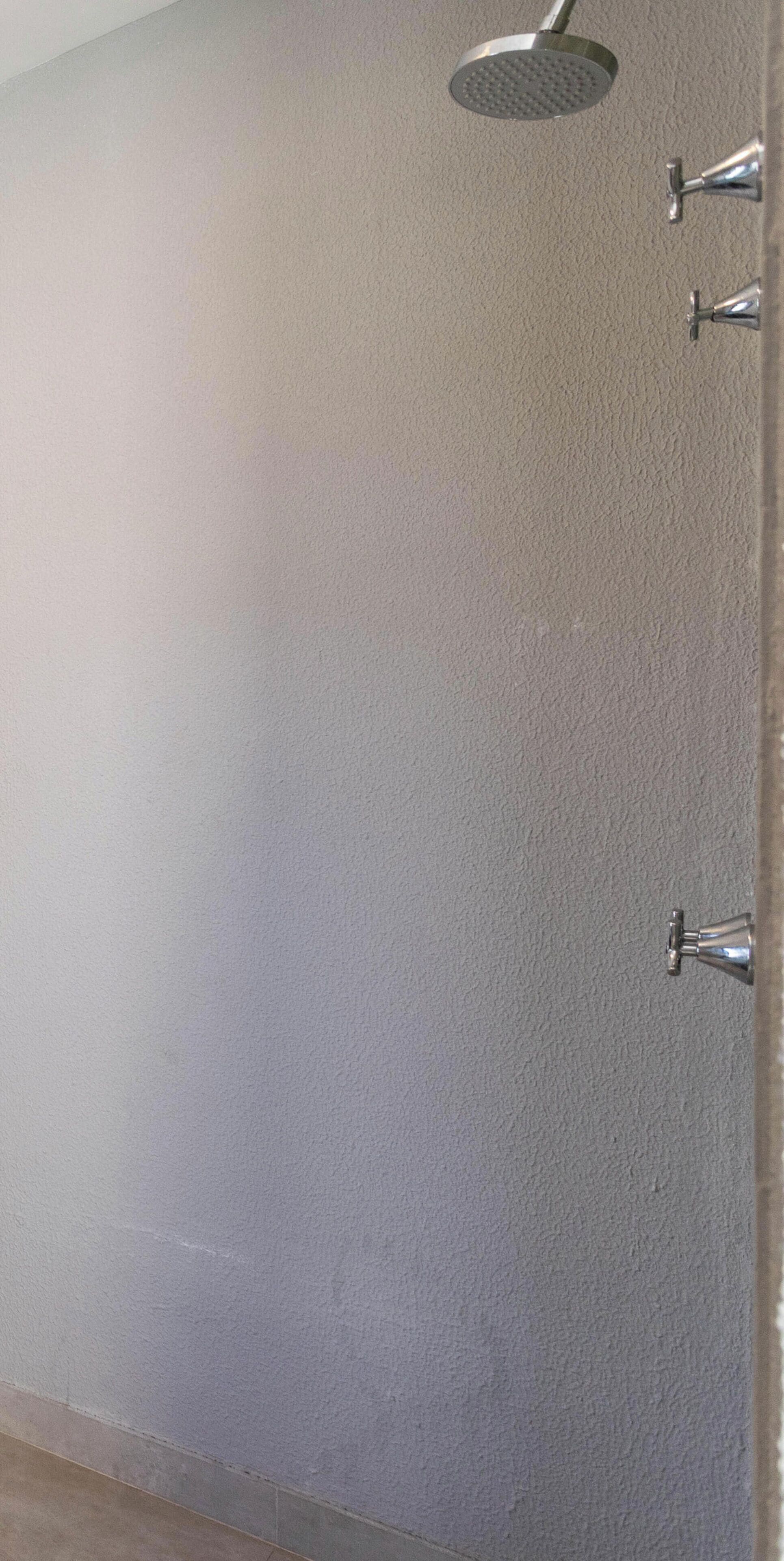A bathroom with a shower head, a wall-mounted faucet, and a tiled floor.