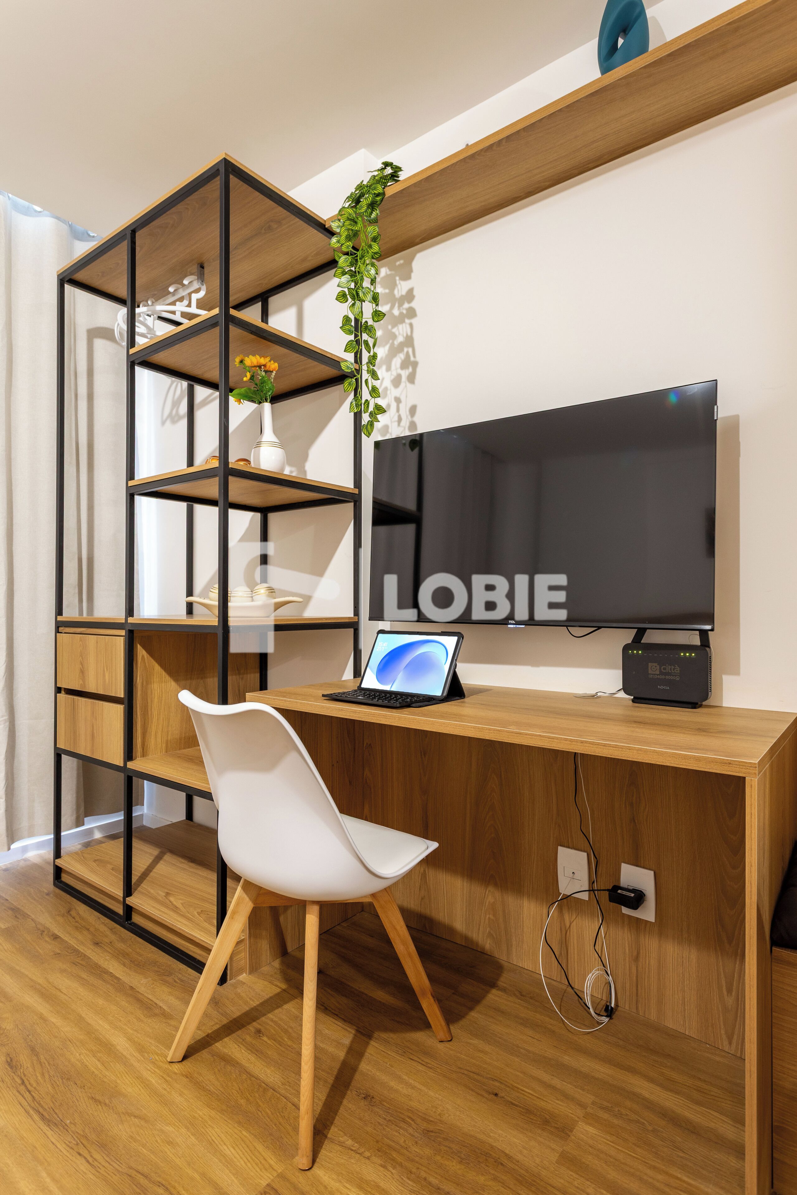 Un espacio de trabajo moderno con un escritorio de madera, una silla blanca, un televisor y una estantería con una planta.