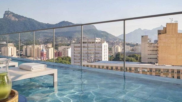 Una piscina infinita con vistas a la ciudad, un área de descanso con mesa y sillas, y un cielo despejado.