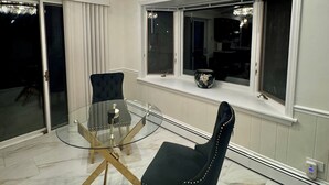 Et spiseområde med et glasbord og stole, en lysekrone og udsigt gennem et vindue.