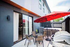 A patio with wicker chairs and a red umbrella, a barbecue grill, and a sliding glass door leading to an indoor area. - 3-bedroom townhome in welcoming Dallas with AC for comfort (Dallas)